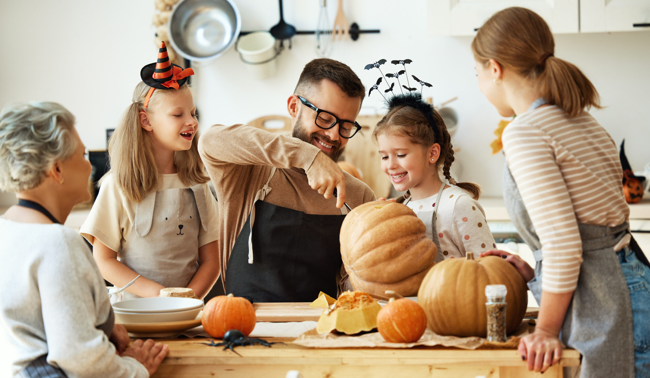 happy family mother, father, grandmother and children prepare for Halloween by carving pumpkins at home in the kitchen