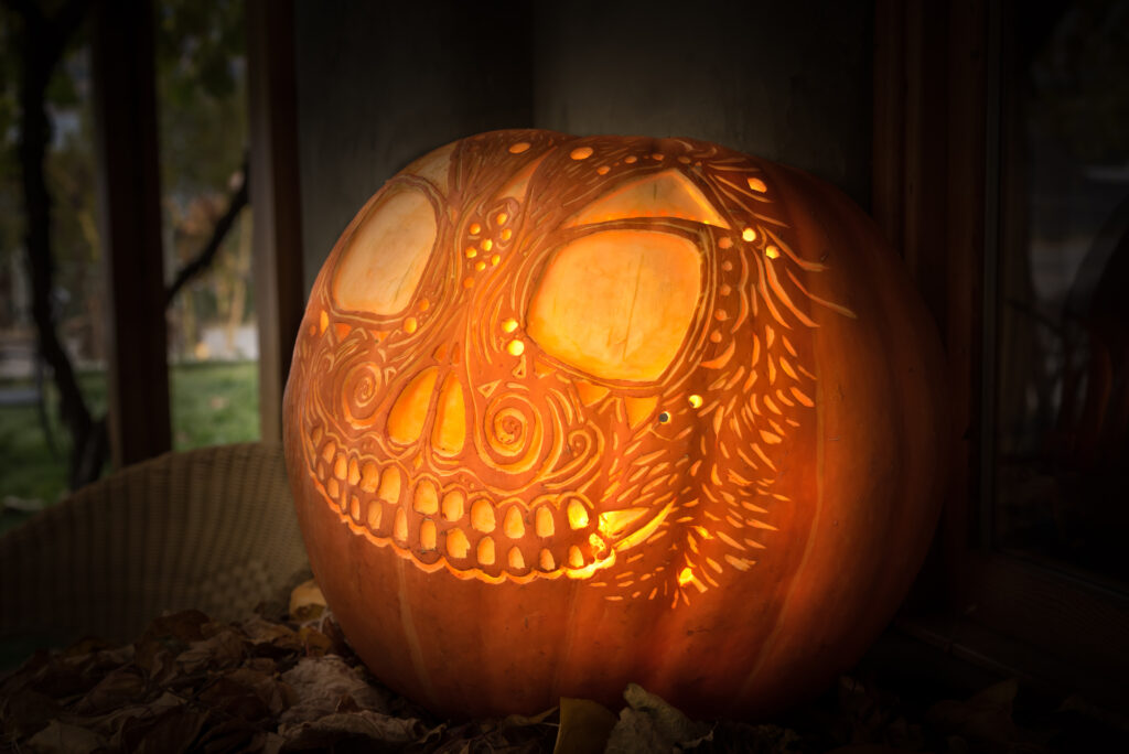 Artistically carved glowing jack-o'-lantern on tabletop display with leaves for Halloween