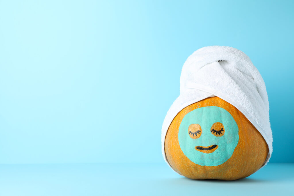 Pumpkin with facial mask and towel on blue background