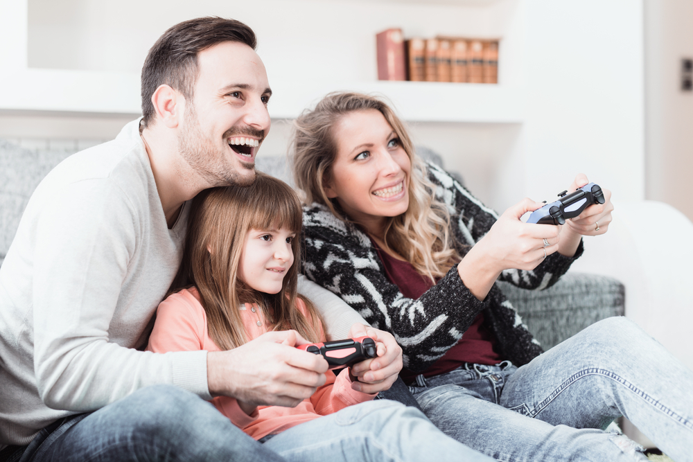 Happy family- father, mother and daughter playing a video game at home.