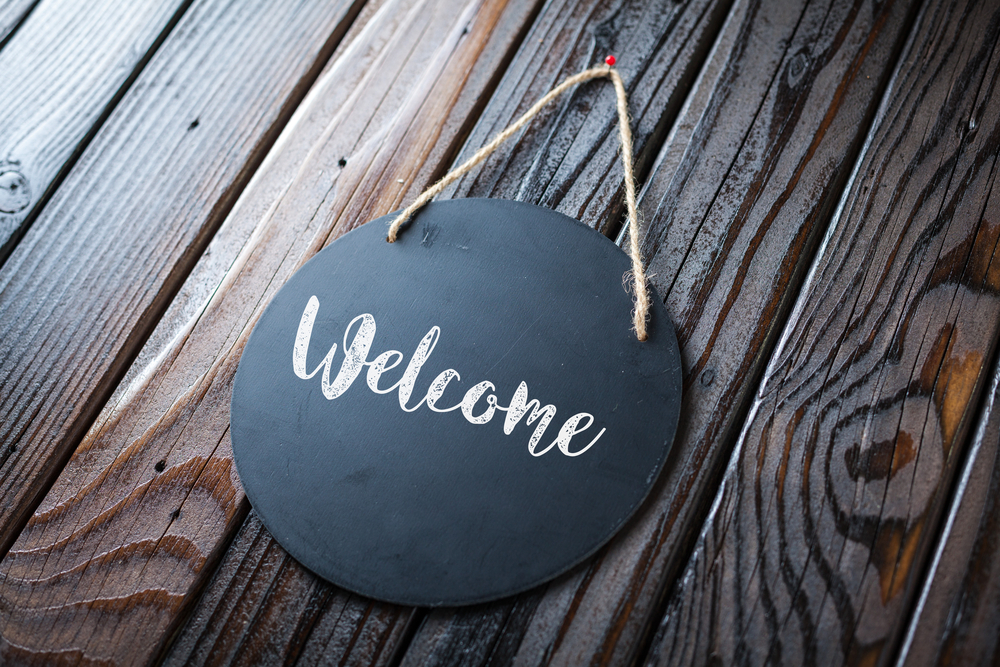 Welcome Sign Written In Chalk On Chalkboard On Rustic Vintage Wood Background. 
