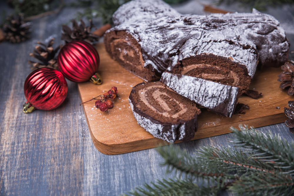 Chocolate yule log Christmas cake is a traditional French Christmas dessert with Mocha cream. Surrounded by fir-tree branches, cones, and berries, and covered in powdered sugar