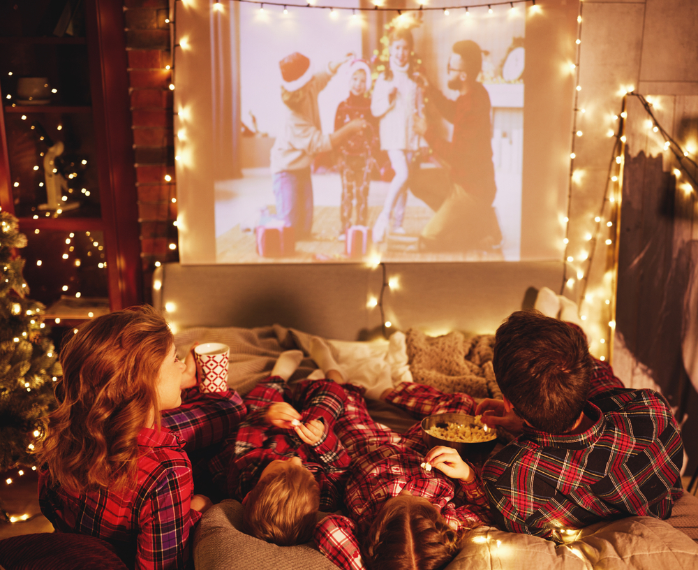 happy family in checkered pajamas: watching projector, film with popcorn in christmas holiday evening at home