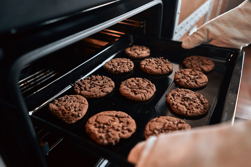 Close up of hands taking out a baking sheet from the oven with cookies with chocolate.