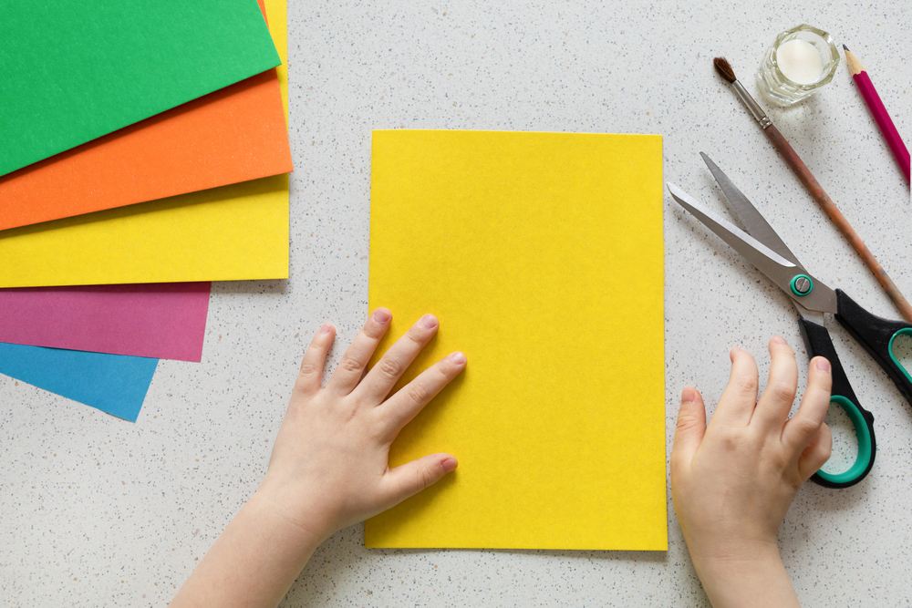 kid making crafts with yellow piece of paper and scissors 