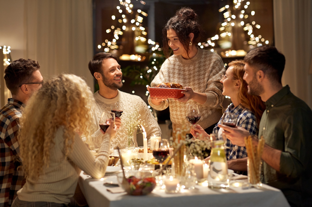 holidays, celebration and people concept - happy smiling friends having christmas dinner at home in evening