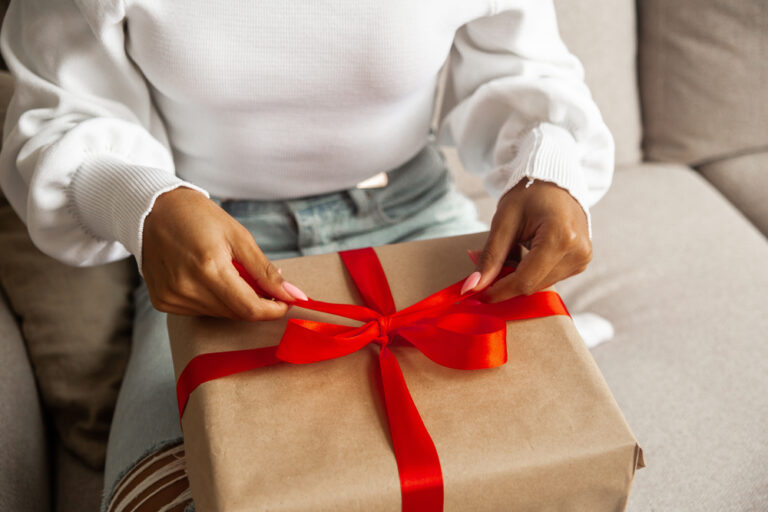 Close up hands of young woman opens box with christmas gift with red ribbon.