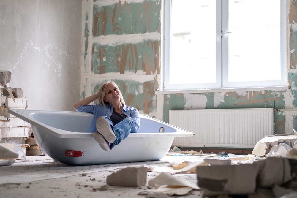 young happy woman sits in bathtub in the middle of the room during home renovation. Empty walls, repairs house with their own hands.