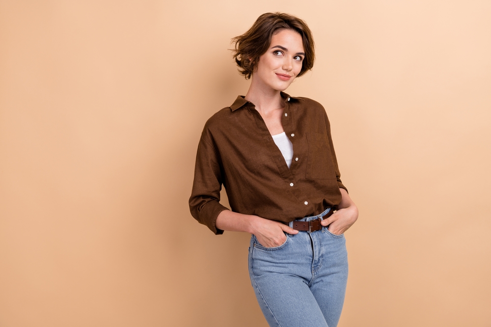 girl with short hairdo wear stylish shirt palms in pockets look empty space isolated on beige color background