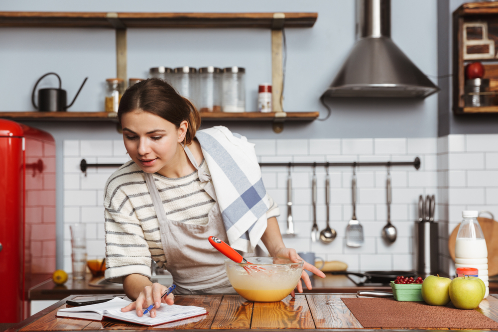 Happy young woman standing at the kitchen at home, mixing eggs in a bowl