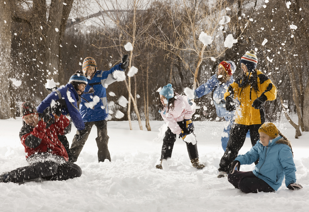 Four people outdors in hats, coats and scarves, having an energetic snowball fight,