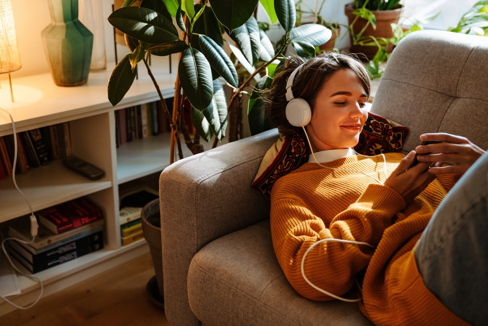 woman listening music and using cellphone while resting on couch at home