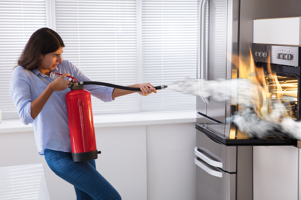 Young Woman Using Fire Extinguisher To Put Out Fire From Oven At Home
