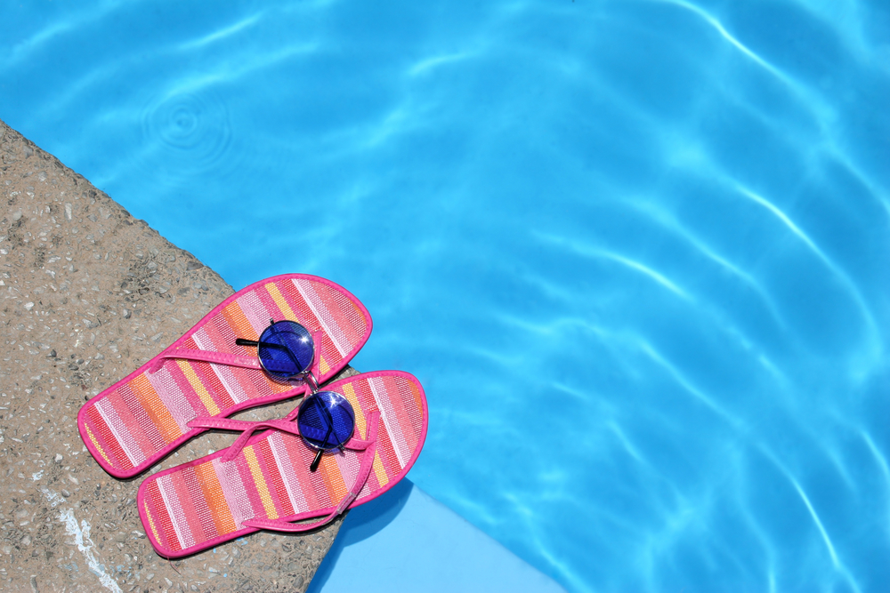 Pink flip-flops and sunglasses by blue pool