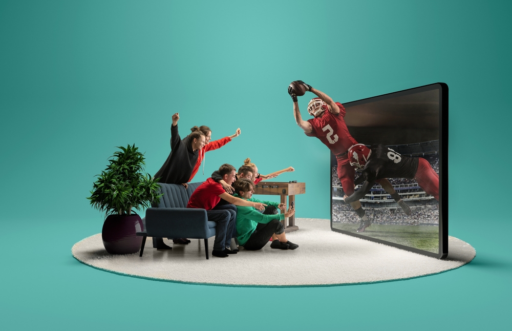 Live stream game. Group of friends sitting in front of huge 3D model of TV screen at home interior and watching online broadcast of american football match. 
