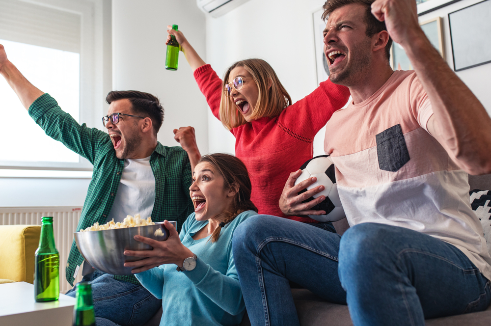 Cheerful friends watching football game at home and cheering for their team.