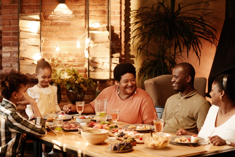 Warm toned portrait of big African-American family sitting at table outdoors and enjoying dinner together at evening