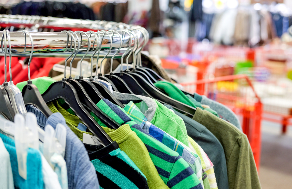 Close-up view of a selection of different used clothes for men, women and children on the rack in a second hand shop or thrift store