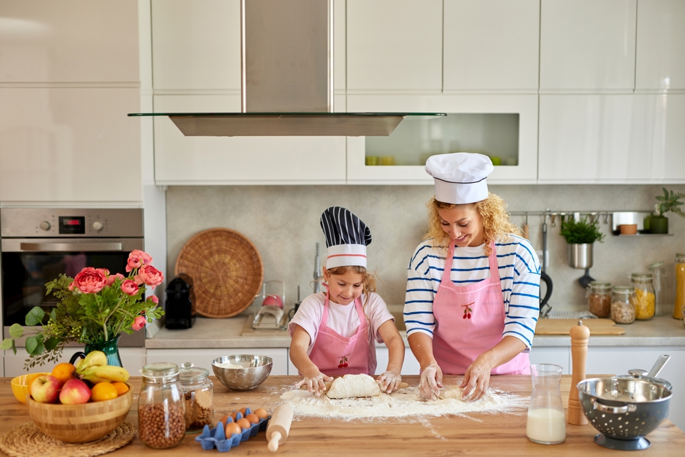 Mother and daughter baking cakes together in the kitchen wearing chefs hats