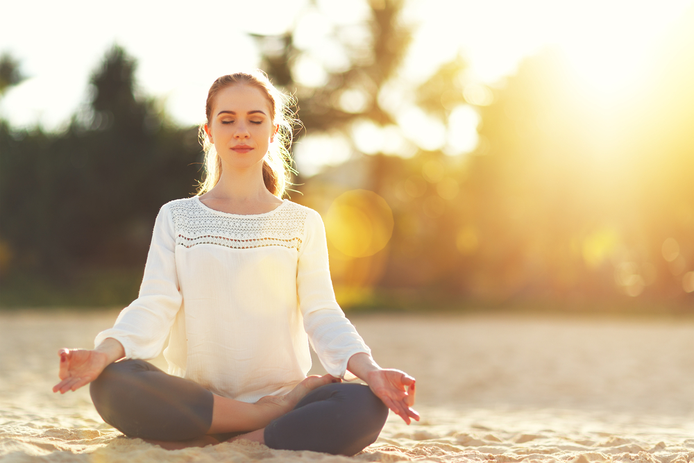 woman practices yoga and meditates in the lotus position on the beach