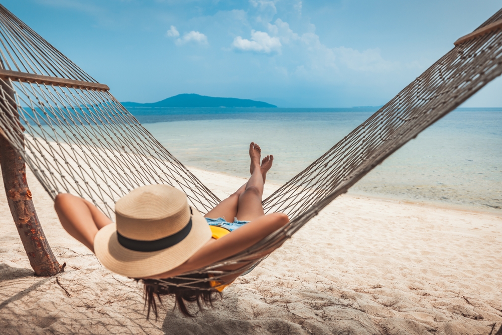 Summer travel vacation concept, Happy traveler asian woman with hat relax in hammock on beach