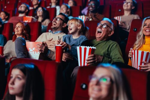 A grandfather and his granddaughter are in the movies enjoying themselves and having fun laughing out loud.