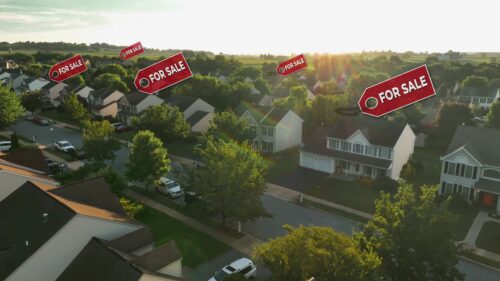 American neighborhood houses with For Sale graphic signs above homes. Aerial view at sunset of real estate market